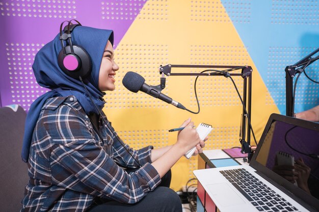 Una donna musulmana eccitata sta registrando un podcast in studio con il laptop