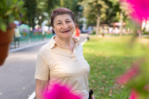 Una donna nel parco cammina nordica con bastoni in una soleggiata giornata estiva. La donna anziana di buon umore è impegnata nell'allenamento mattutino.