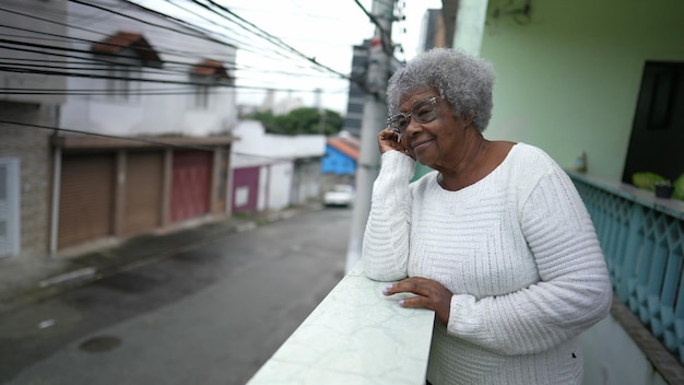 Una donna nera anziana che guarda fuori dal balcone di casa guardando il quartiere