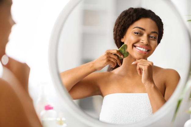 Una donna nera attraente che massaggia il viso con un raschiatore di pietra gua sha