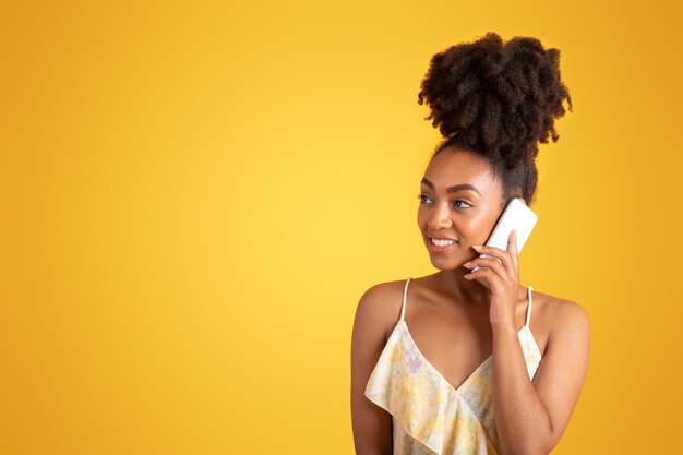 Una donna nera millenaria felice che chiama per telefono pensando guarda lo spazio vuoto