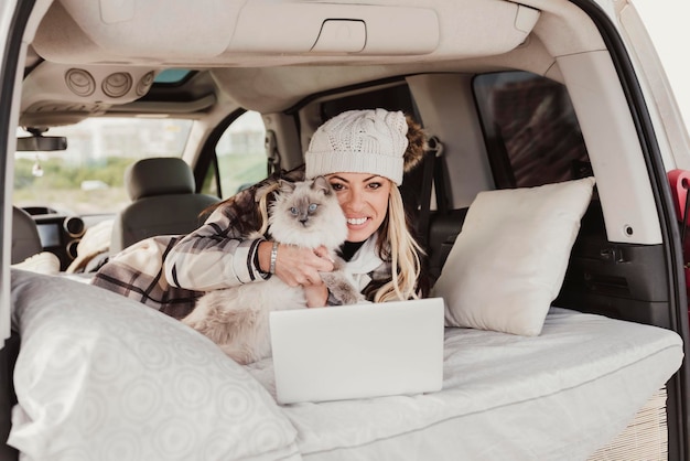 Una donna nomade digitale in camper con in mano un gatto che guarda la telecamera e utilizza il laptop guardando la telecamera Concetto di stile di vita delle persone moderne e libertà dei nomadi digitali