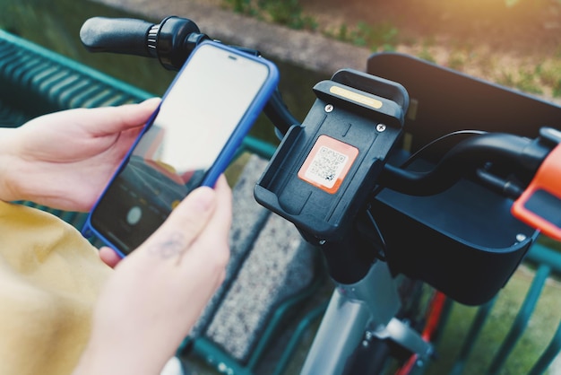 Una donna prende una bicicletta a noleggio in un parcheggio per biciclette con uno smartphone