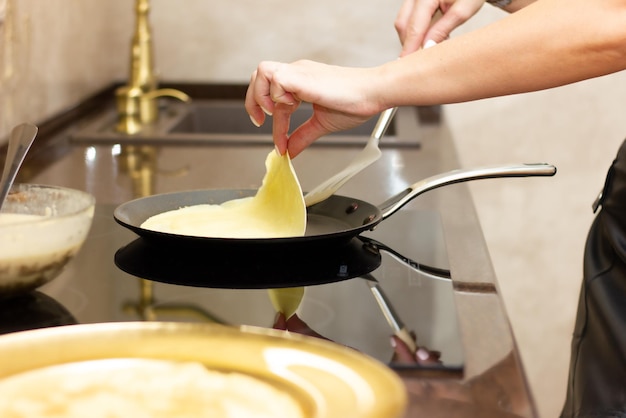 Una donna prepara frittelle russe in cucina un primo piano su una padella