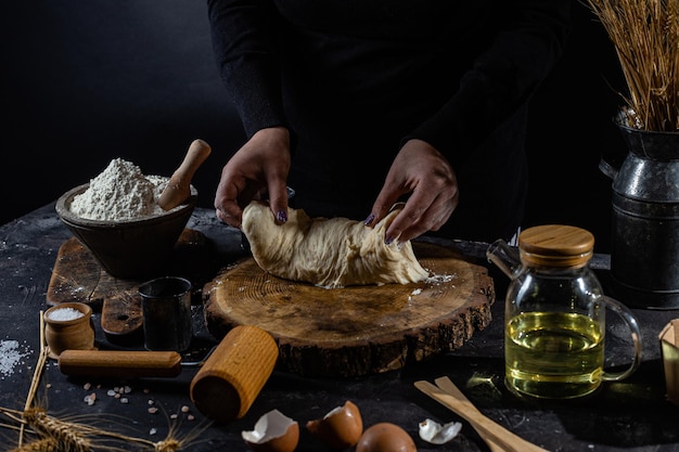 Una donna prepara la pasta su un tavolo scuro. Farina, pasta lievitata, sfondo scuro