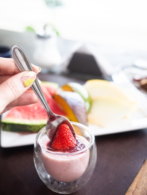 Una donna prepara un dessert a base di yogurt alla fragola con qualche fetta di frutta fresca