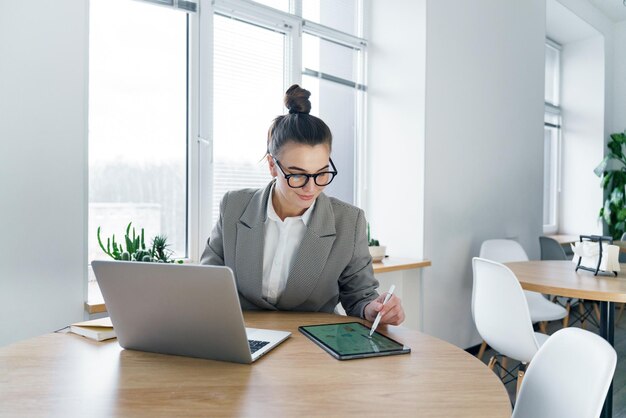 Una donna professionale diligente si concentra sul suo tablet utilizzando lo stilo lavoro di precisione con il suo portatile