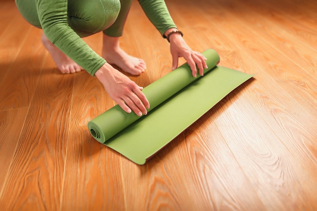 Una donna raccoglie un tappetino verde dopo una lezione di yoga.