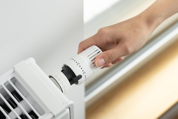 Una donna regola il termostato del radiatore sulla modalità economica di riscaldamento dell'ambiente