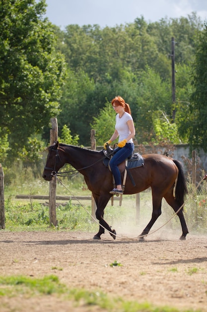 Una donna rossa a cavallo in una foresta di fattoria sullo sfondo