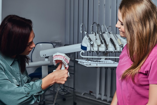 Una donna rossa seduta su una poltrona del dentista e che tiene la dentiera in uno studio dentistico.