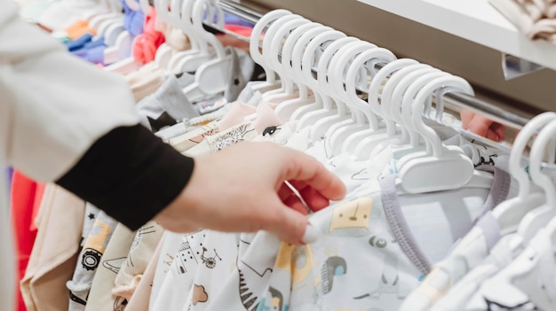 Una donna sceglie i vestiti per bambini in un negozio di abbigliamento per bambini Gravidanza e shopping