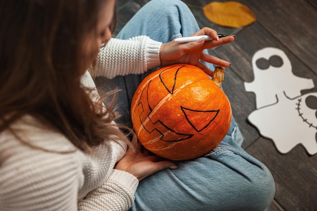 Una donna seduta su un pavimento di legno dipinge una faccia di zucca e fa Jack Latern per Halloween