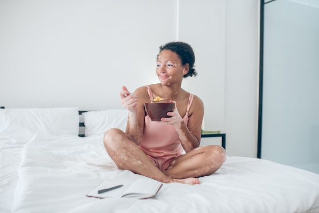 Una donna seduta sul letto e facendo colazione