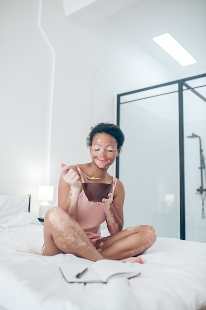 Una donna seduta sul letto e facendo colazione