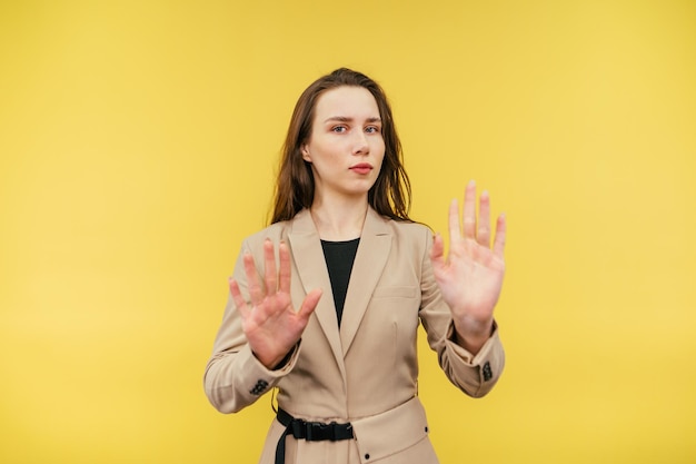Una donna seria in abiti casual eleganti si trova su uno sfondo giallo e mostra l'arresto del gesto dei palmi