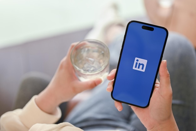 Una donna si rilassa seduta in un bar e usa l'applicazione LinkedIn sul suo telefono