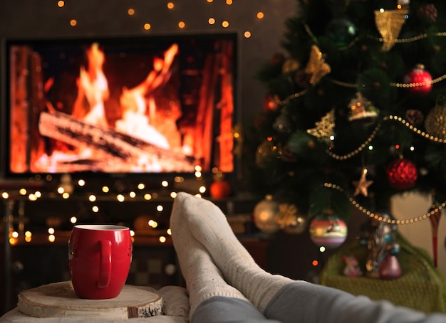 Una donna si scalda i piedi con i calzini davanti al caminetto con una tazza di bevanda calda Concetto di vacanze invernali