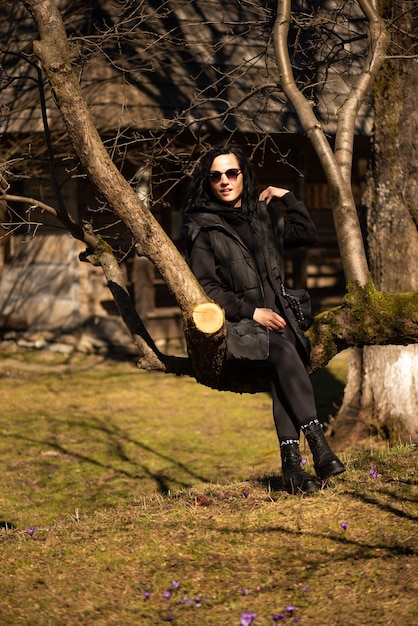 Una donna si siede su un ramo di un albero in un parco.