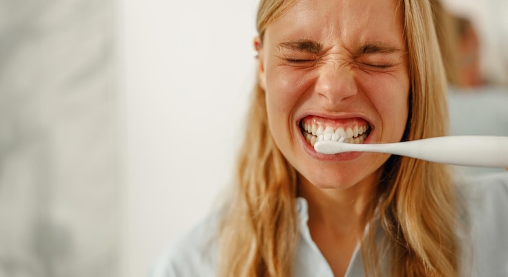 Foto una donna si sta spazzolando i denti con uno spazzolino da denti elettrico in uno spazio da bagno in stile moderno