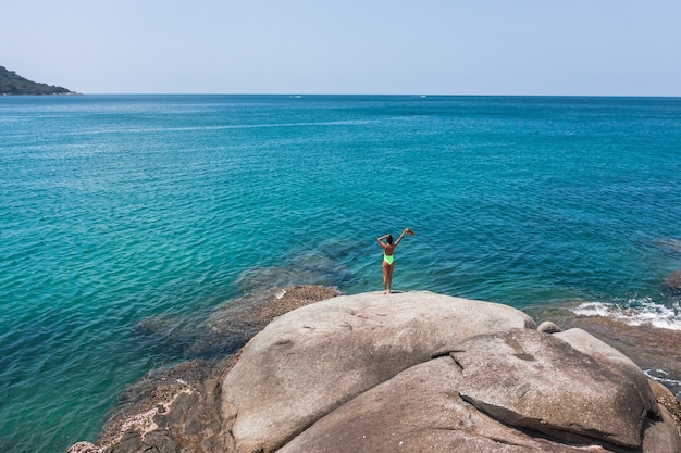 Una donna si trova su una roccia e ammira l'azzurro del mare