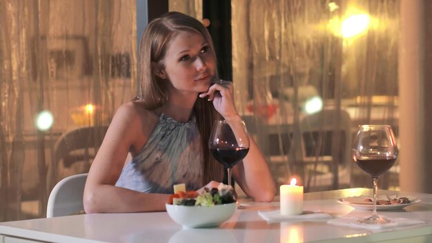 Una donna siede a un tavolo con un bicchiere di vino e una candela sullo sfondo