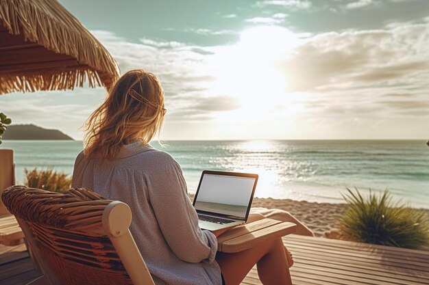 una donna siede su una spiaggia con un computer portatile e un tramonto sullo sfondo