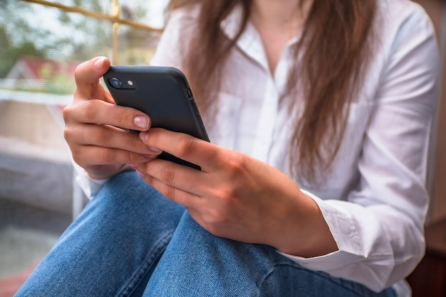 Una donna siede sul davanzale di una finestra con in mano un telefono con la parola telefono sullo schermo.