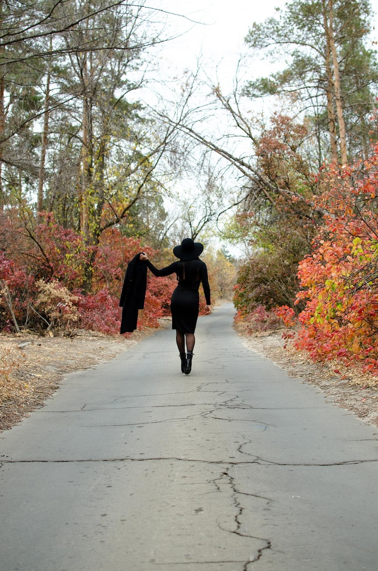 Foto una donna snella con un cappotto nero e un cappello in un parco autunnale cammina lungo la foto della strada dal retro