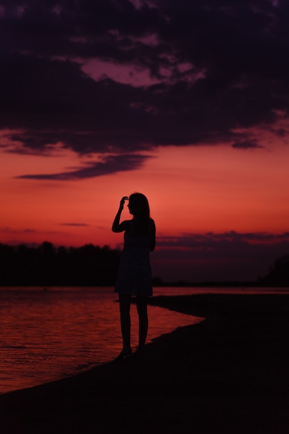 Una donna snella è in piedi sulla spiaggia una bella giovane donna felice ammira il tramonto e solleva...