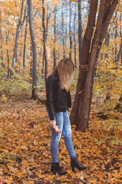 Una donna sola e triste sta prendendo a calci le foglie gialle in un umore triste autunnale e in un concetto di disturbo affettivo stagionale