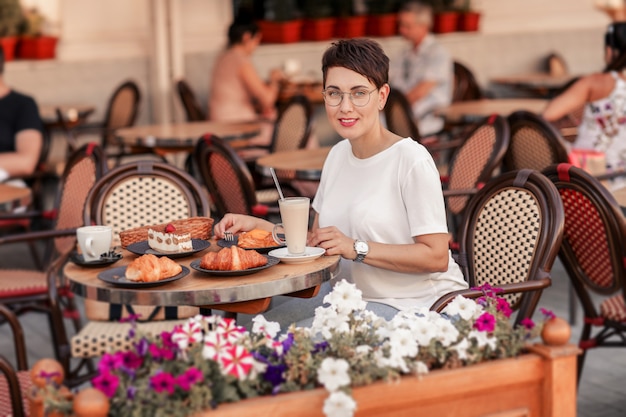 Una donna sorride e beve caffè e torte in un caffè europeo di strada