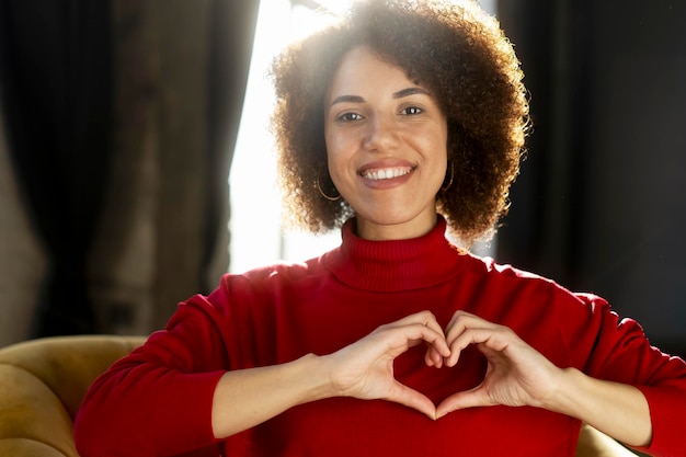 Una donna sorridente che indossa un maglione rosso che fa un cuore con le mani guardando la fotocamera