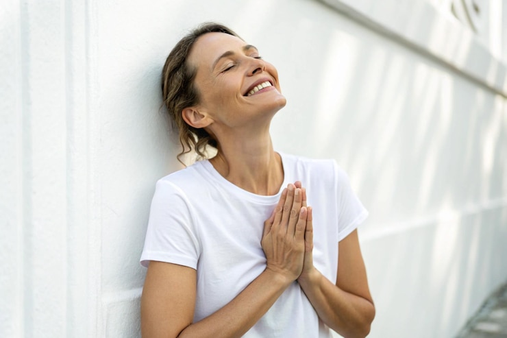 Foto una donna sorridente con gli occhi chiusi e le mani abbracciate sul petto sullo sfondo bianco