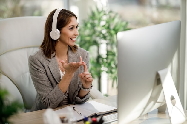 Una donna sorridente con le cuffie che lavora al computer nel suo ufficio a casa.