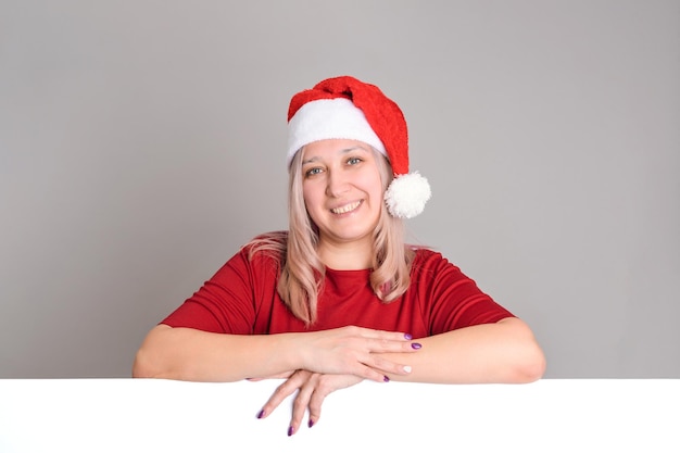 Una donna sorridente con un cappello da Babbo Natale appoggia le mani su una tavola vuota vuota