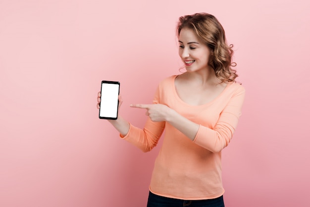 Una donna sorridente tiene in mano un telefono e punta il dito verso uno schermo bianco. Isolato.