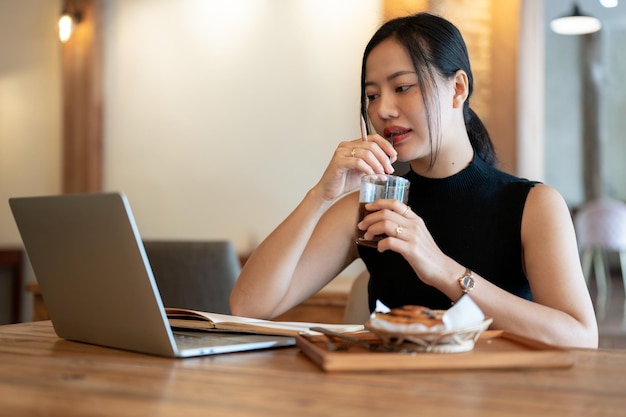 Una donna sorseggia un caffè mentre guarda lo schermo del suo laptop mentre lavora in remoto in un bar