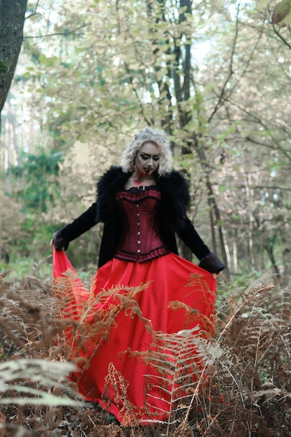 Una donna sotto forma di vampiro o strega in abito medievale cammina nella foresta