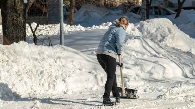 Una donna spala la neve da un marciapiede.