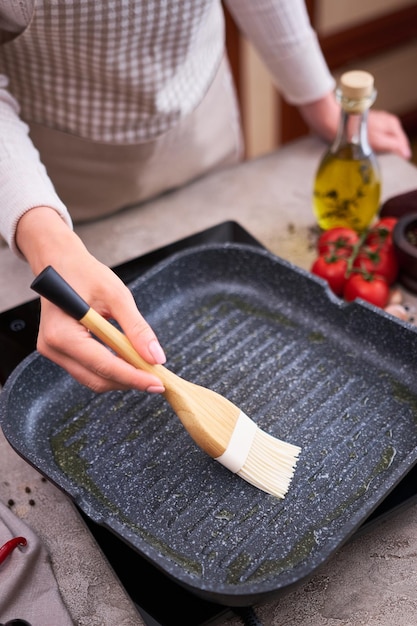 Una donna spalma l'olio d'oliva sulla padella per grigliare con una spazzola in silicone nella cucina domestica