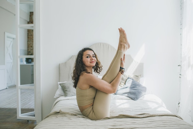 Una donna sportiva che fa yoga, esegue l'esercizio Paripurna Navasana, posa di equilibrio, a casa o in uno studio di yoga con pareti bianche.