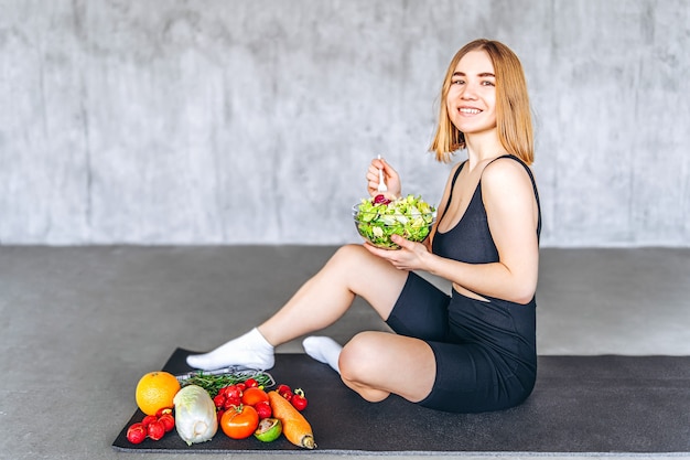 Una donna sportiva in abbigliamento sportivo è seduta sul pavimento con cibo sano.