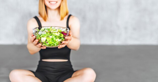 Una donna sportiva in abbigliamento sportivo è seduta sul pavimento con cibo sano.