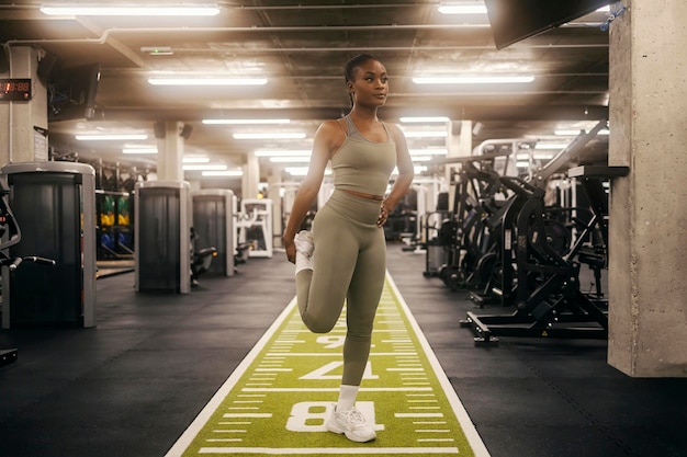 Una donna sportiva nera in forma si allunga le gambe in palestra.