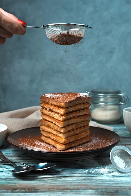 Una donna spruzza il cacao sui waffle su uno sfondo grigio-blu.