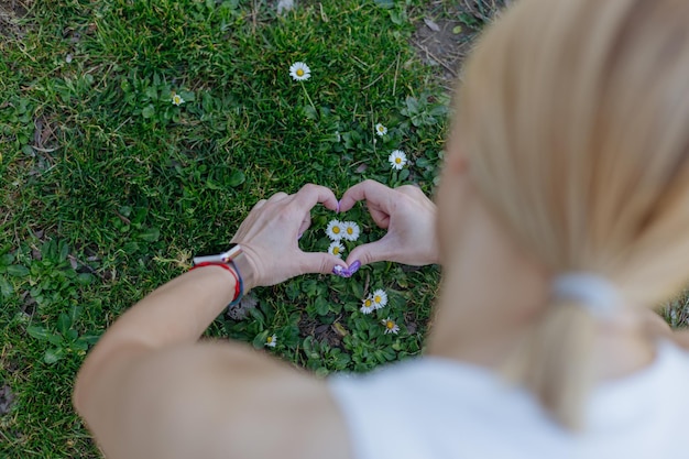 Una donna sta facendo un cuore con le mani nell'erba.