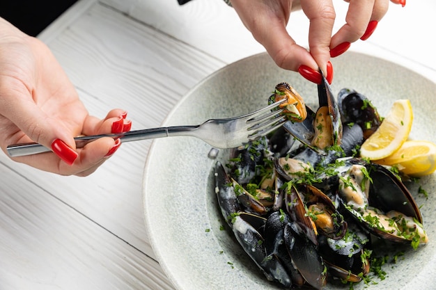 Una donna sta mangiando cozze con una forchetta e un piatto di cozze.