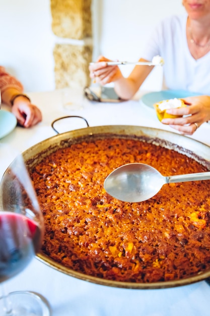 Una donna sta mangiando una paella con un bicchiere di vino rosso sullo sfondo.