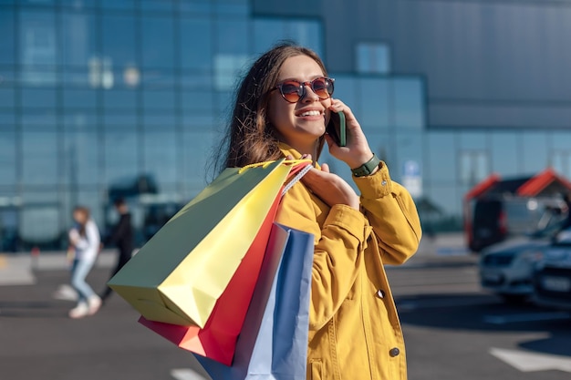 Una donna sta parlando al telefono e tiene delle borse sulla spalla